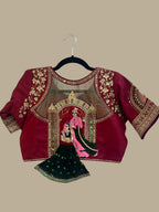 House Of Indian Wedding Attire maroon silk-like blouse with gold embroidery and sheer yoke, paired with a dark green skirt.